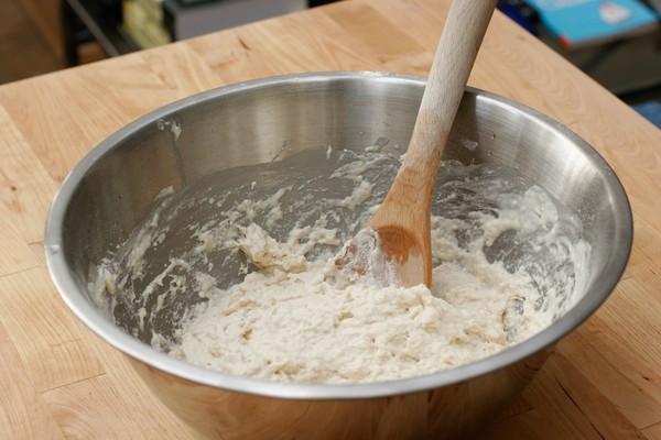 A metal mixing bowl with dough and a wooden spoon in it