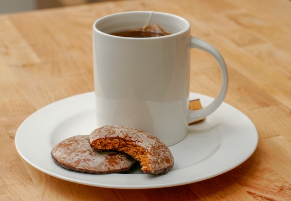 A cup of tea with two holiday spice cookies on the saucer; one cookie has a bite taken out of it