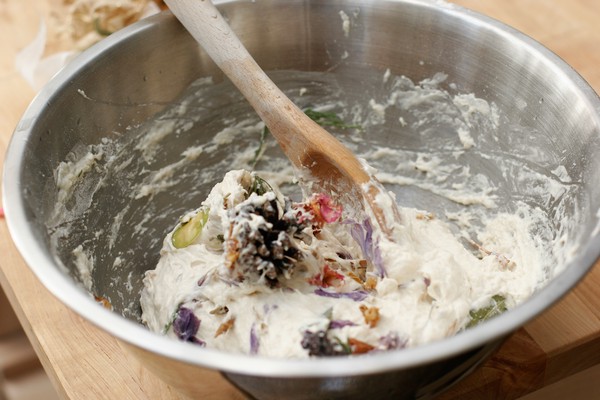 Dough, lumpy with large potpourri chunks, being mixed with a wooden spoon in a metal mixing bowl
