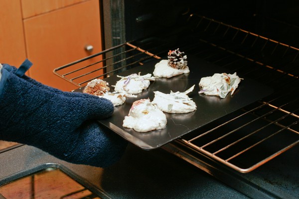 A hand wearing an oven mitt putting a cookie sheet with cookie dough into an oven