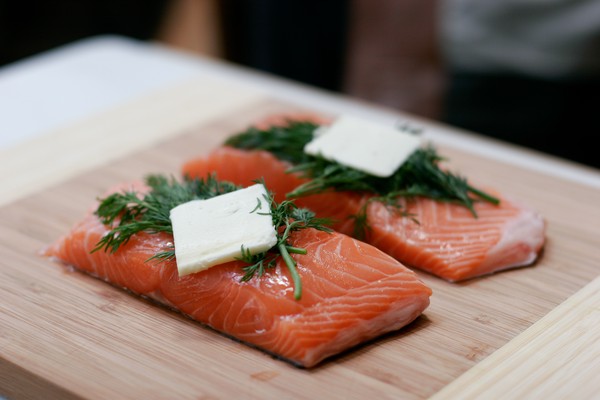 Two strips of salmon topped with dill, tarragon, and a pat of butter on a wooden cutting board