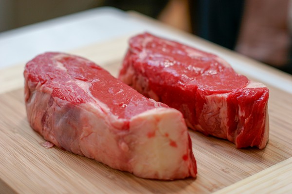 Two New York strip steaks on a wooden cutting board