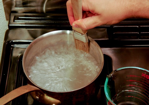 A human hand placing the tip of a paintbrush into a pot of boiling liquid