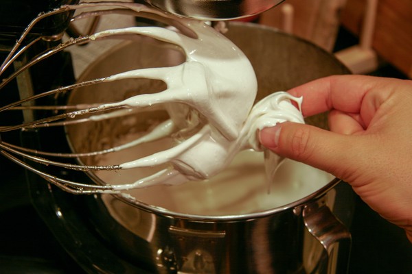 Pinching the nougat A human hand pinching something white that is on a stand mixer whisk above a stand mixer bowl, which contains something white