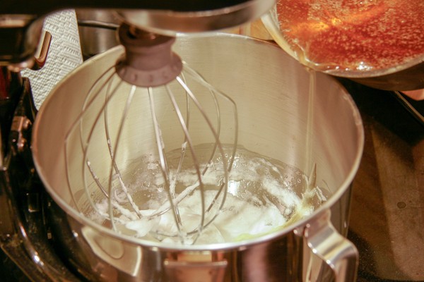 A pot of brown liquid being poured into a stand mixer bowl, which contains something white