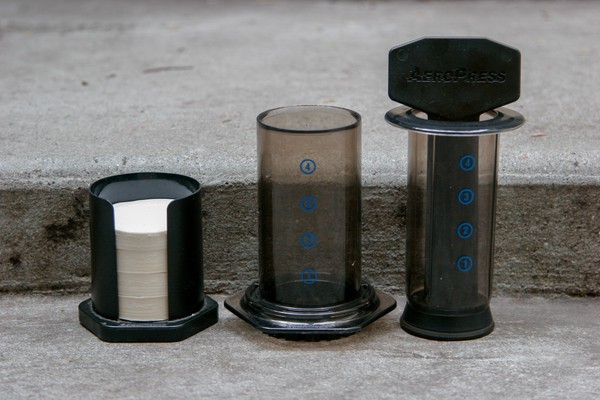 The components of an AeroPress® standing on a concrete step