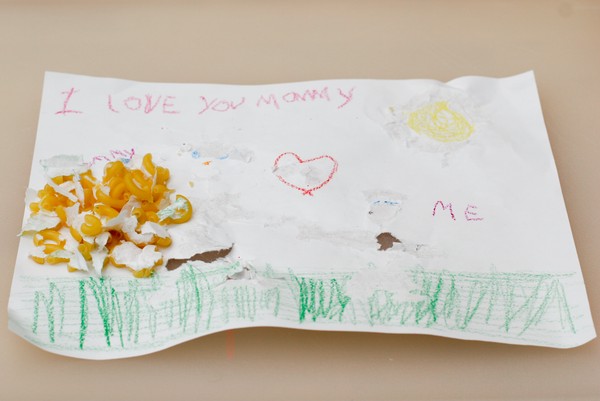 A pile of macaroni that has been scraped off of a macaroni art drawing; the pile is sitting on what remains of the drawing