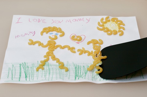 A spatula scraping macaroni off of a macaroni art drawing