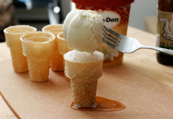 A scoop of vanilla ice cream on a fork, being lowered onto an ice cream cone filled with root beer