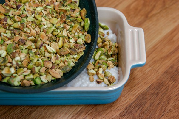Pistachios in a pan, being poured onto a chicken skin stretched across the bottom of a small, rectangular baking dish