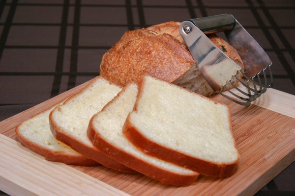 A pastry blender resting on a half of a loaf of sourdough bread with four perfect slices of white bread in the foreground