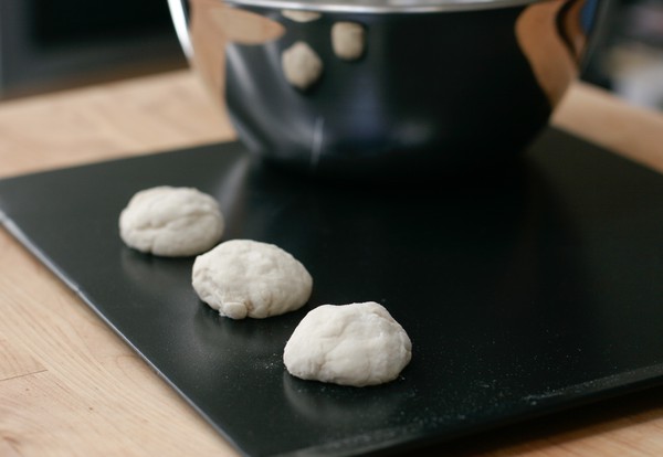 Three mounds of light-colored cookie dough on a cookie sheet with a metal bowl in the background