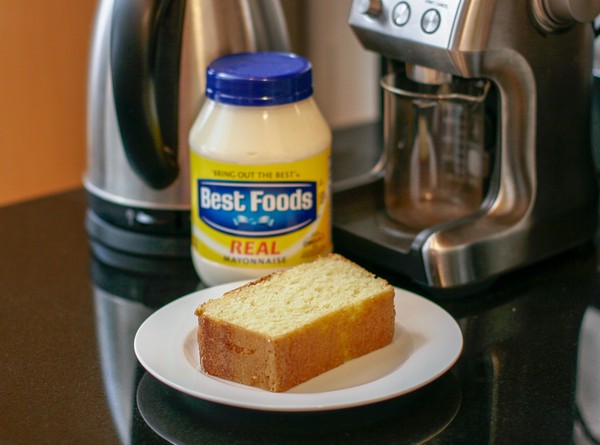 Shawnique's moist lemon cake A slice of yellow loaf cake on a white plate with a jar of mayonnaise in the background, along with a coffee grinder and electric kettle