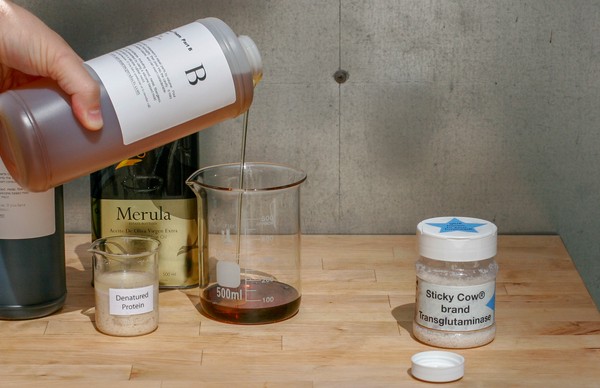 Bottle of unknown substance labeled, 'B' being poured into large beaker with other bottles/beakers nearby
